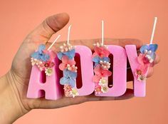 a hand holding three candles that spell out the word aoy with flowers on them