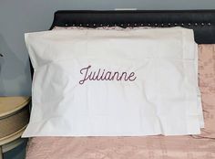 a white pillow with the word juliane on it sitting on a bed next to a night stand