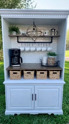 an open cabinet with baskets and coffee maker on top, sitting in the grass next to a brick wall