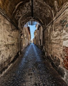 an alley way with cobblestone pavement and brick walls on both sides, leading into the distance