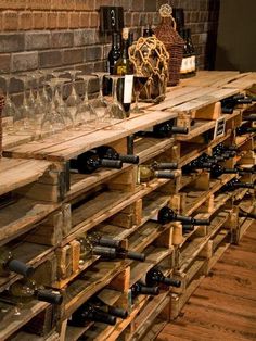 wine bottles and glasses are lined up on wooden shelves in front of a brick wall