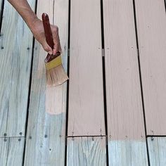 a person with a paint brush on a wooden decking area that has planks and boards