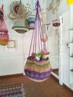 several hanging baskets in a room with wood flooring and white walls, one is filled with colorful crocheted items