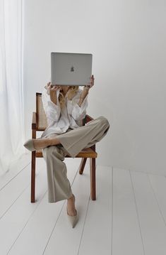 a woman sitting in a chair holding up a laptop