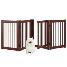 a small white dog sitting in front of a wooden gate with two open gates on each side