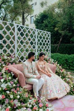 the bride and groom are sitting on a pink couch in front of some pretty flowers