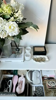 an organized drawer with shoes, jewelry and flowers in it on a white table top