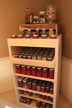 a wooden shelf filled with jars and jams on top of a floor next to a wall