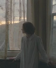 a woman standing in front of a window with her hands on the windowsill looking out