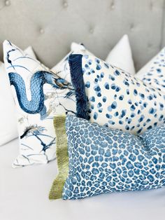 four different pillows on a white bed with blue and green designs, one in the shape of a dragon