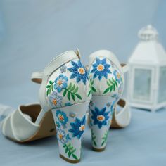 a pair of white shoes with blue and yellow flowers on them next to a lantern