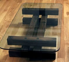 a glass coffee table with wooden legs and a square shaped design on the top, sitting on a hard wood floor