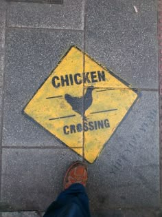 a chicken crossing sign on the ground next to a person's feet and shoes