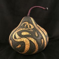 a black and gold pear shaped vase with a handle on it's side, sitting on a black background