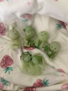 three little green toy animals sitting on top of a white bed sheet covered in pink flowers