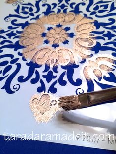 a paintbrush is sitting on top of a blue and white paper with gold designs