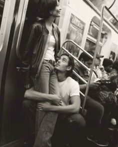 two people sitting on a subway car with their arms around each other as they look up at the sky