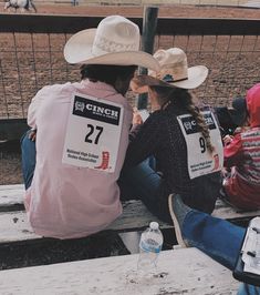 two people wearing cowboy hats sitting on a bench at a horse race, one is holding a water bottle