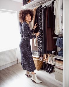 a woman standing in front of a closet full of clothes and shoes with her hand on the hanger