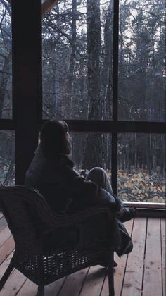 a person sitting on a chair in front of a window looking out at the woods