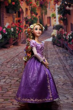 the doll is wearing a purple dress with flowers on it's head and holding a flower in her hand