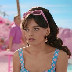 a woman wearing pink sunglasses and a blue polka dot dress sitting in front of a pool