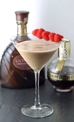 a martini with raspberries on the rim next to a bottle of booze