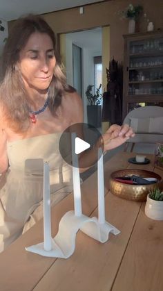 a woman standing in front of a wooden table with two white candles on top of it