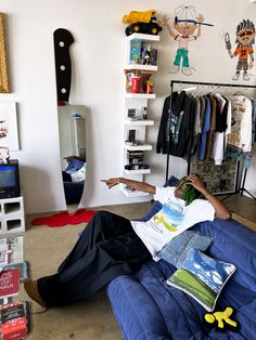 a man laying on top of a blue couch in a room filled with books and toys