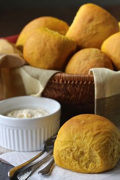 bread, butter and spoons sit on a table next to a basket of rolls