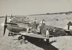 an old black and white photo of men standing next to two airplanes on the grass