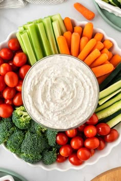 a bowl filled with dip surrounded by veggies, tomatoes, celery and carrots