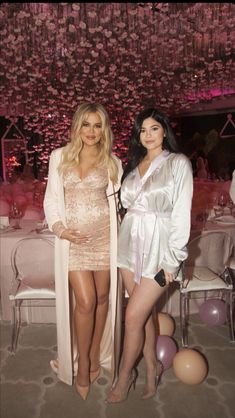 two beautiful women standing next to each other in front of balloons and chandeliers