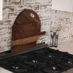 a stove top oven sitting inside of a kitchen next to a white brick wall and wooden cutting board