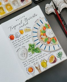 an artist's notebook with watercolors and paints on the table next to it