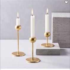 three candles are sitting next to each other on a white table with a gray wall in the background