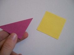 a hand holding a piece of paper next to an origami triangle on a white surface