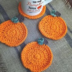 three crocheted pumpkin coasters sitting next to a coffee cup