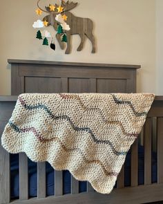 a crocheted blanket hanging from the side of a wooden crib in front of a deer head