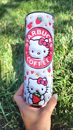 someone holding up a hello kitty coffee can in the grass with strawberries on it