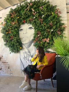 a woman sitting in a chair next to a wall with a large painting on it