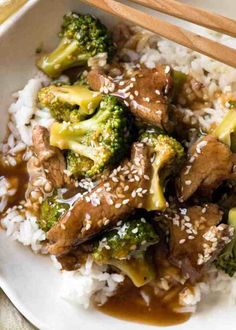 beef and broccoli stir fry on rice with chopsticks in a white bowl