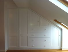 an attic bedroom with white cabinets and wood flooring on the bottom half of the room