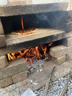 a pizza is cooking in an outdoor brick oven with flames coming out from the top