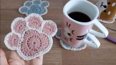 a hand holding a crocheted coaster next to a cup of coffee on a wooden table