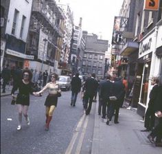 people are walking down the street in an old fashion district, with tall buildings on either side