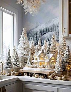 a kitchen counter topped with christmas trees and snow covered houses next to a window sill