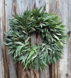 a wreath is hanging on the side of a wooden fence with greenery around it