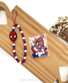 a spiderman beaded necklace next to a package of beads on a wooden board