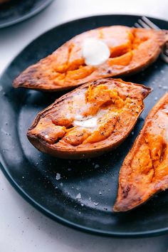 three baked sweet potatoes on a black plate with a fork and knife next to them